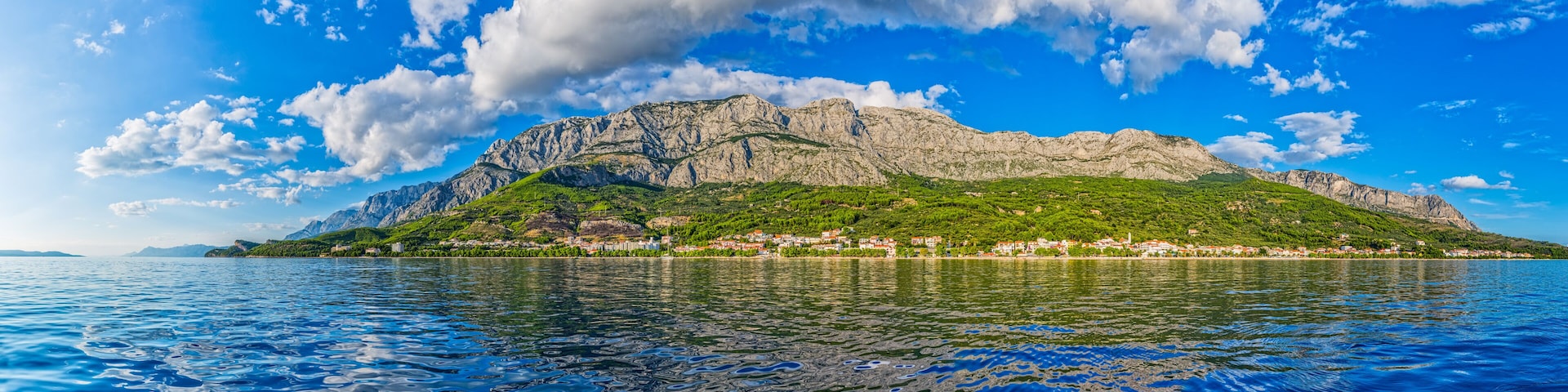 A mountainous island with a village, surrounded by a calm sea under a partly cloudy sky.
