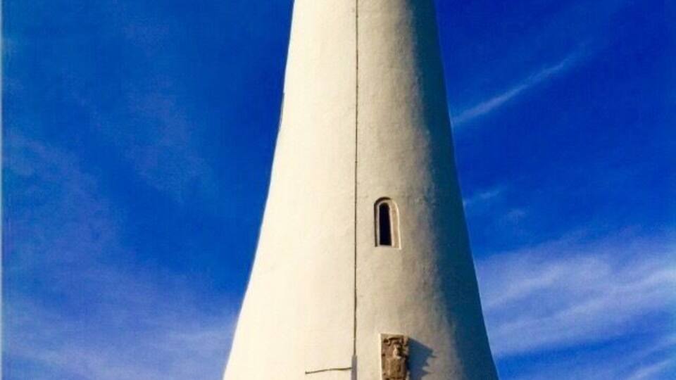 A tall white lighthouse with a dark top against a blue sky.