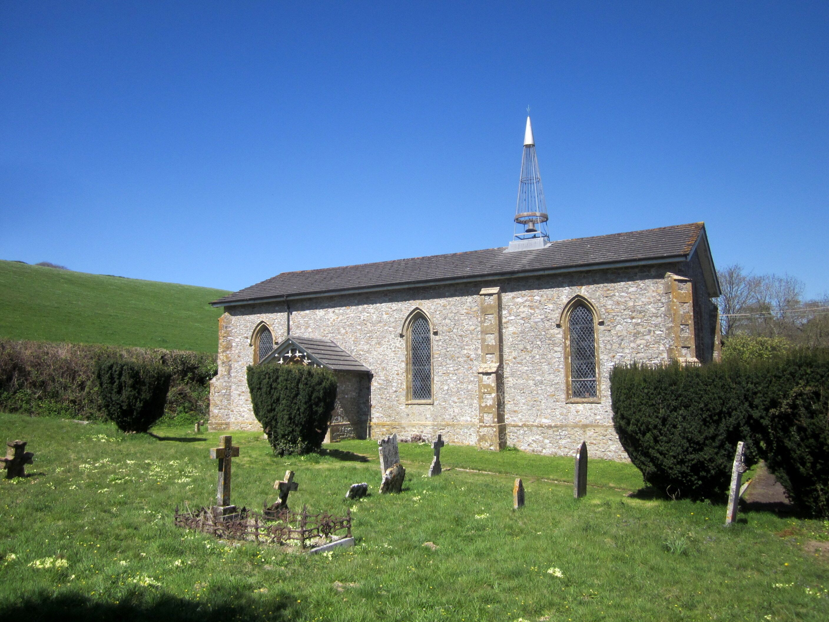 A stone church with a steeple and crosses in a grassy cemetery.