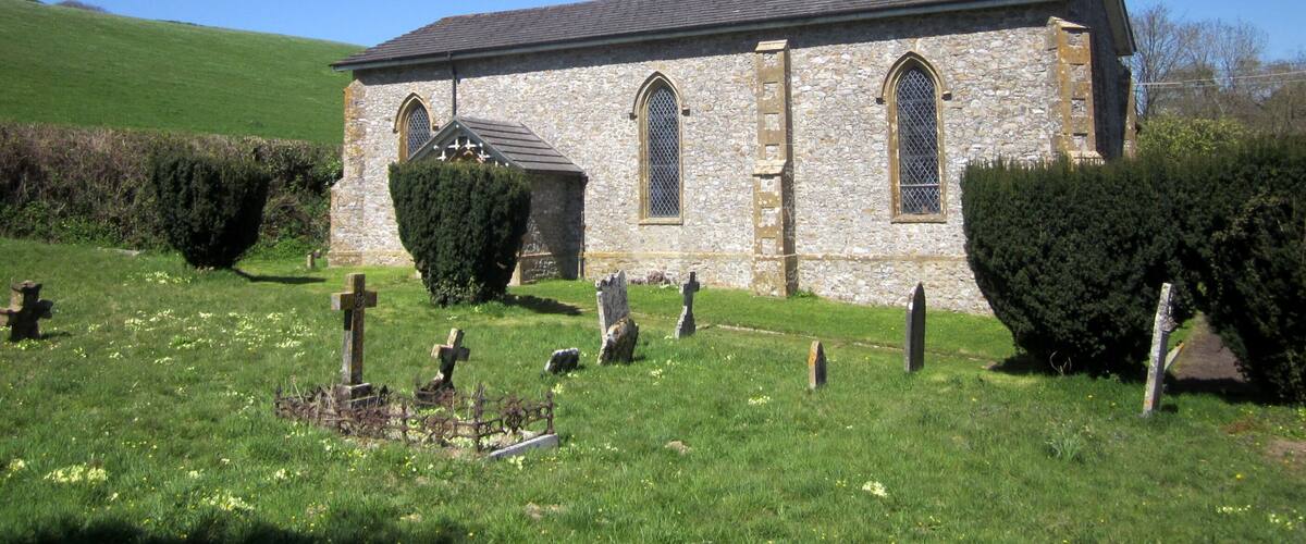 A stone church with a steeple and crosses in a grassy cemetery.