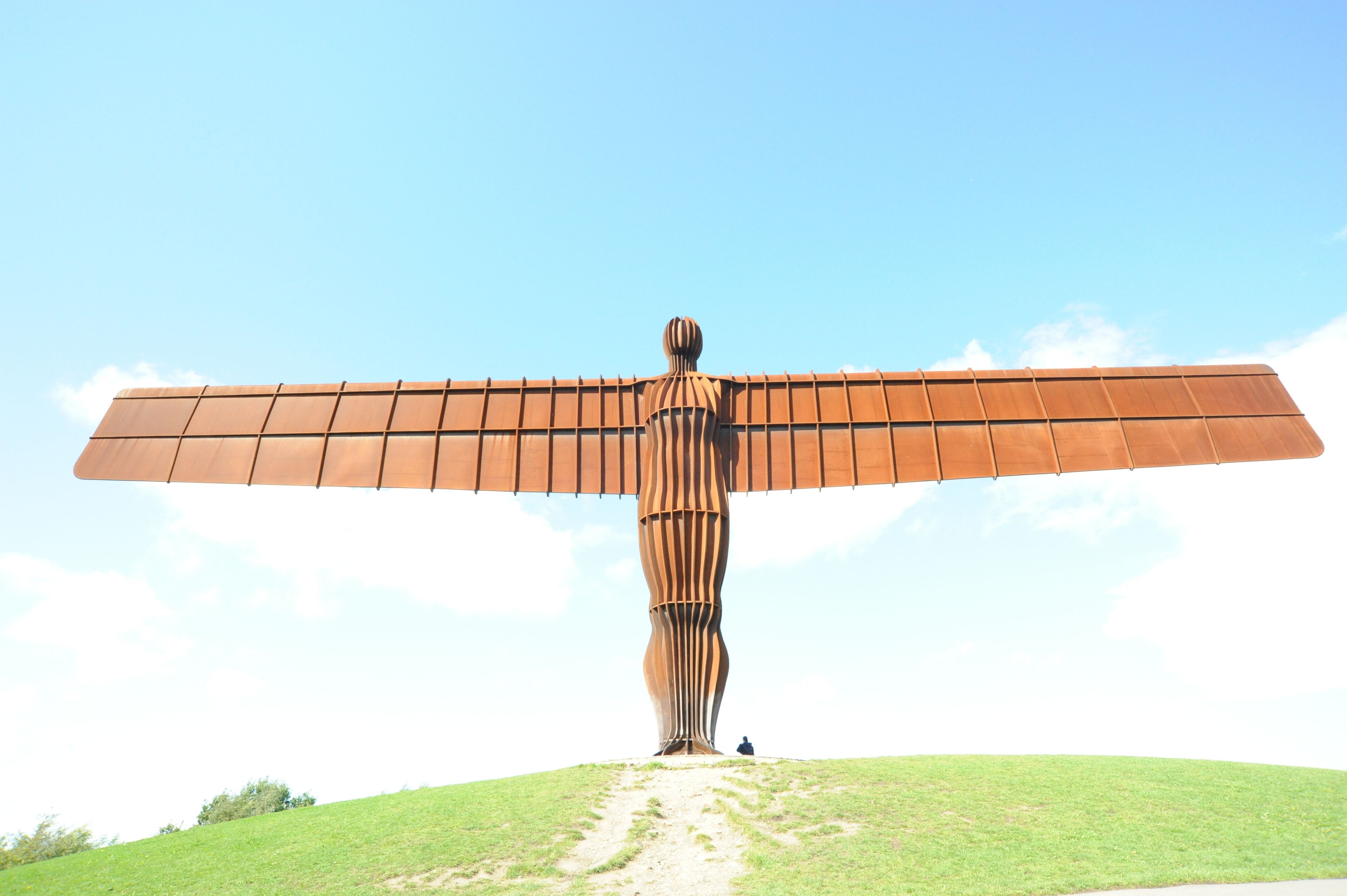 A large metal sculpture with wings on a grassy hill.