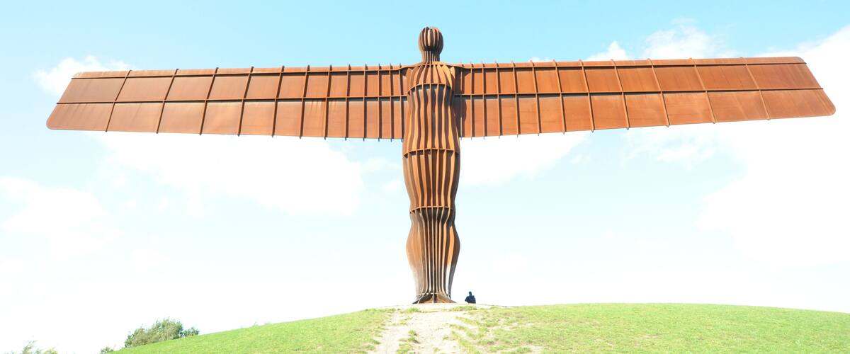 A large metal sculpture with wings on a grassy hill.