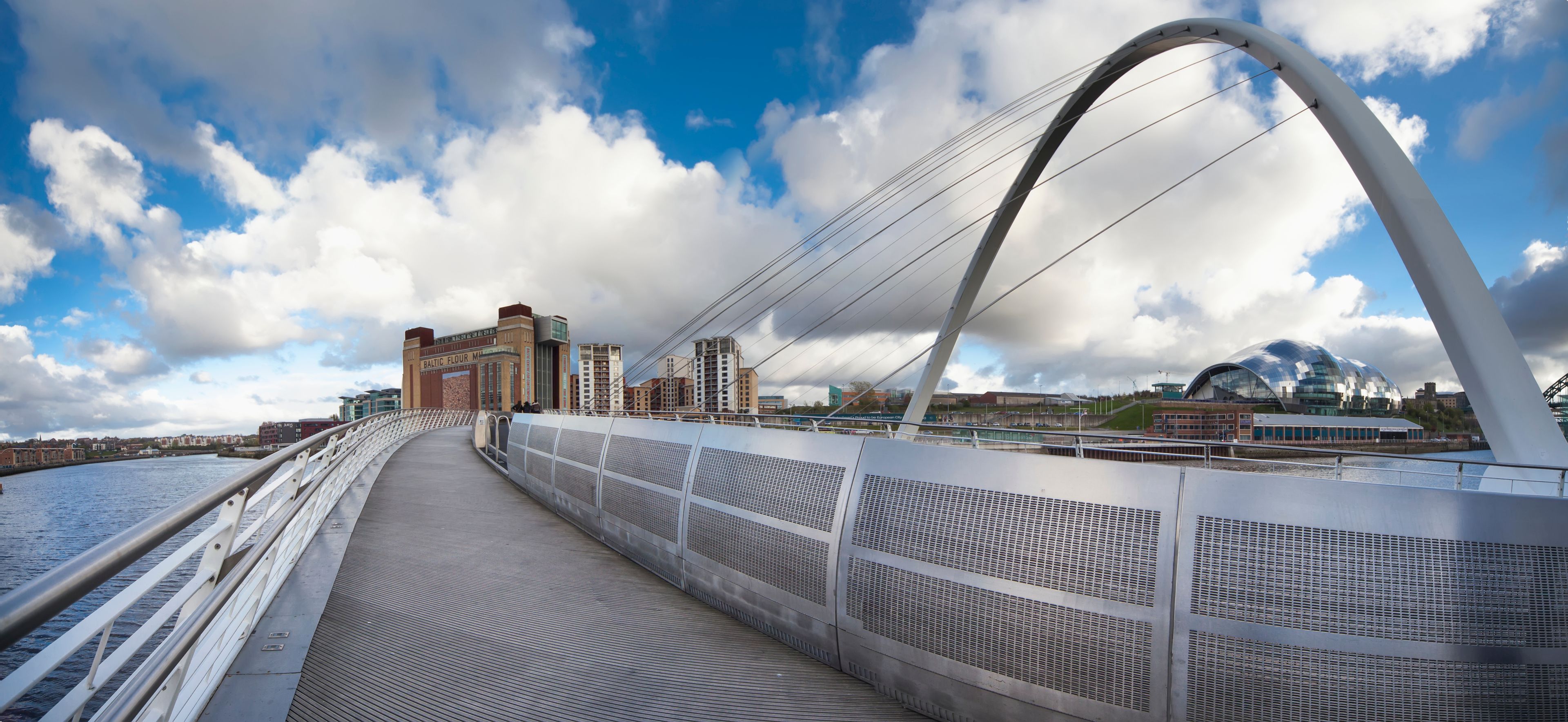 A modern bridge with a curved arch, metal railings, and a river below.