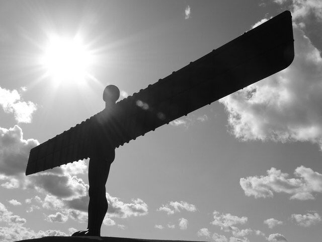 Una persona sostiene una gran estructura parecida a un ala contra un sol brillante y un cielo nublado.