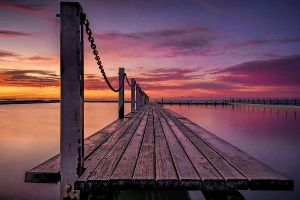 A wooden pier extending into calm water with a sunset sky.