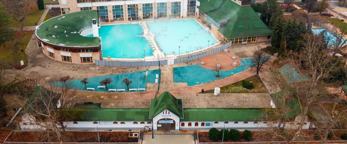 An aerial view of a large building with a swimming pool, surrounded by trees and a park area.