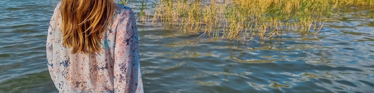 Tourist woman standing at idyllic lakeshore with panoramic view of calm Balaton lake seen from tourist town Balatonmariafurdo, Hungary, Europe. Tranquil serene atmosphere. Travel destination in summer
