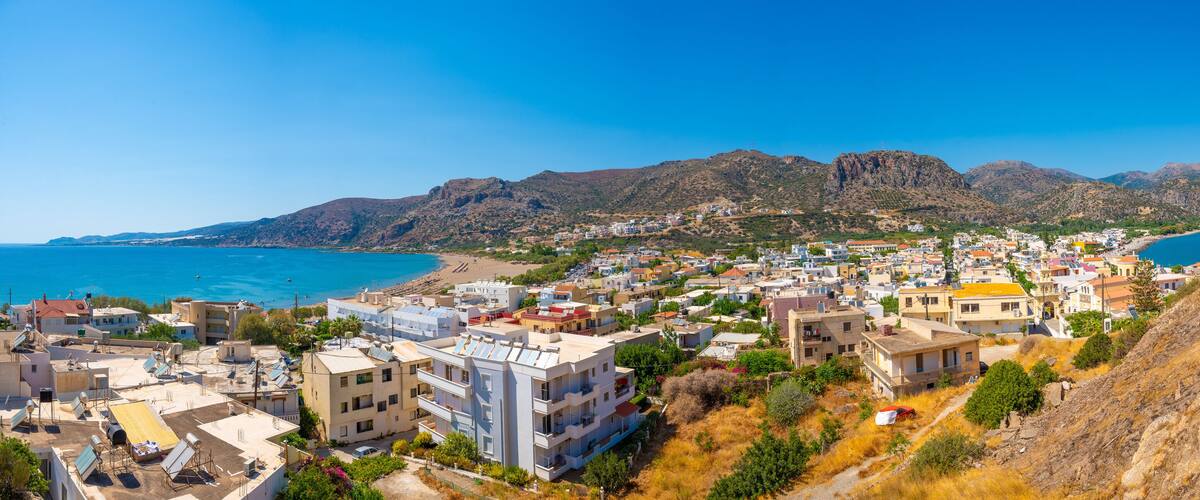 A coastal town with buildings, a beach, and mountains in the background.