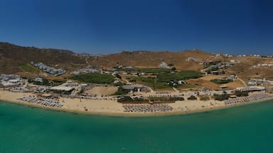 A coastal town with a beach, clear turquoise waters, and hilly terrain in the background.