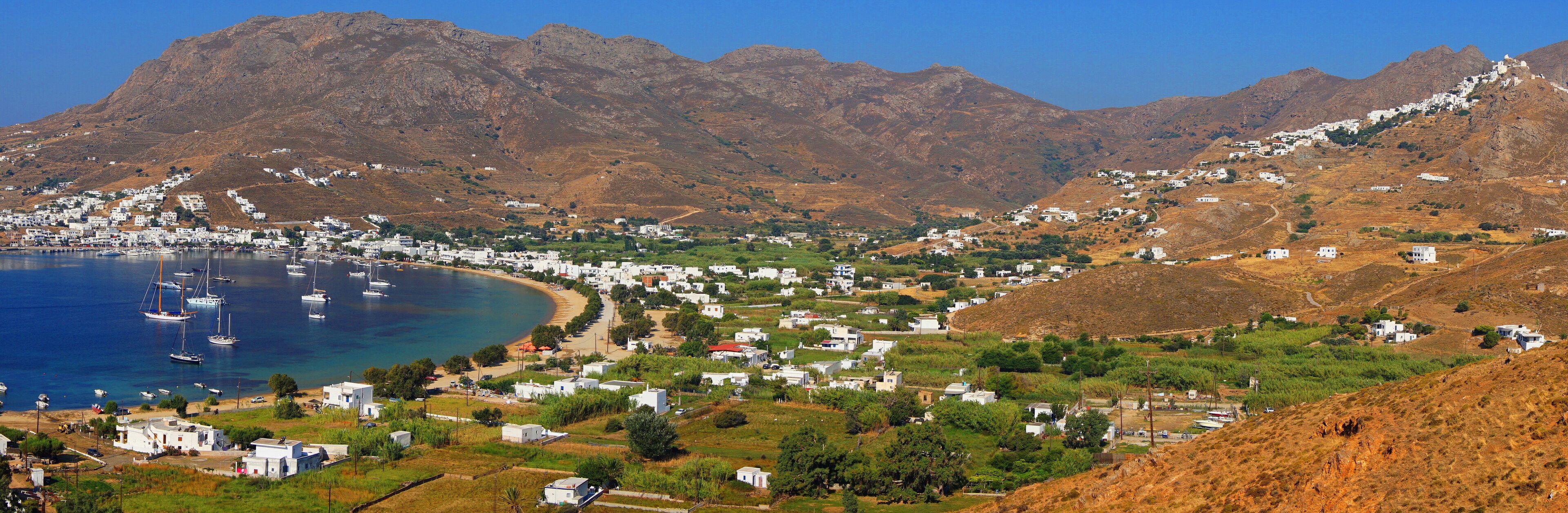 A coastal town with white buildings, a beach, and mountains in the background.