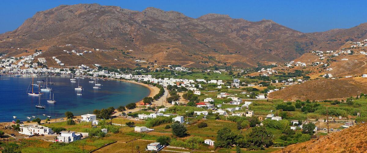 A coastal town with white buildings, a beach, and mountains in the background.