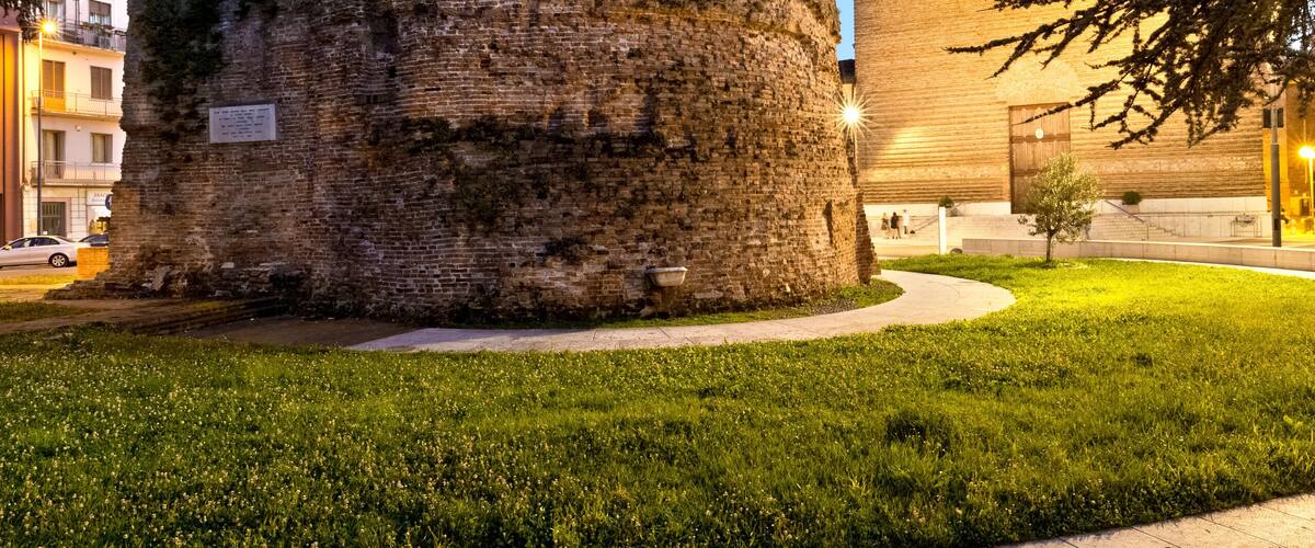 A historic stone tower with a circular top, surrounded by a well-maintained grassy area and a paved walkway.