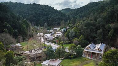 A rural village with houses surrounded by dense forest and hills.