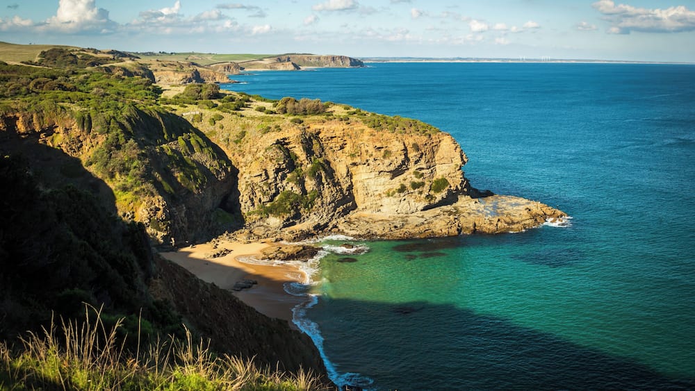 A coastal landscape with cliffs, a sandy beach, and clear blue waters.