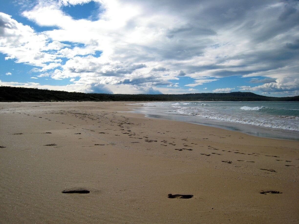 A sandy beach with footprints and waves approaching the shore under a partly cloudy sky.