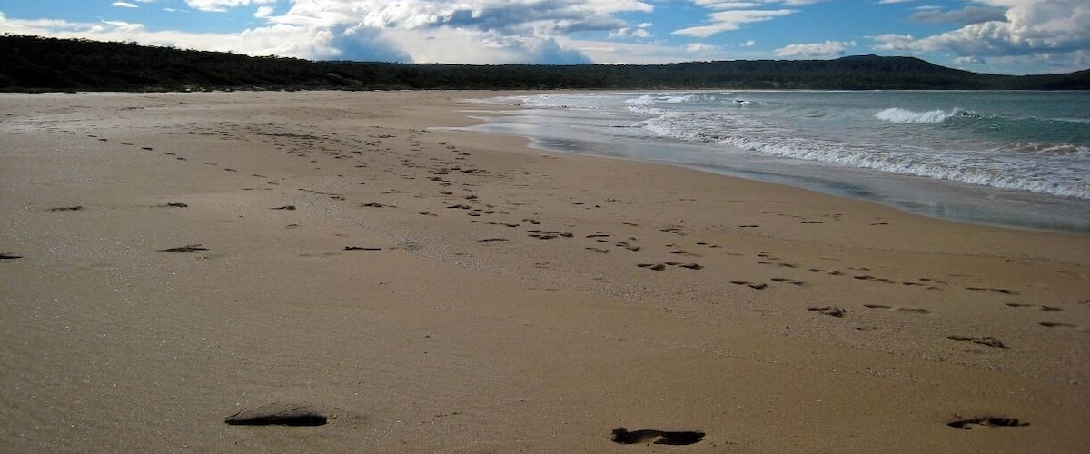 A sandy beach with footprints and waves approaching the shore under a partly cloudy sky.