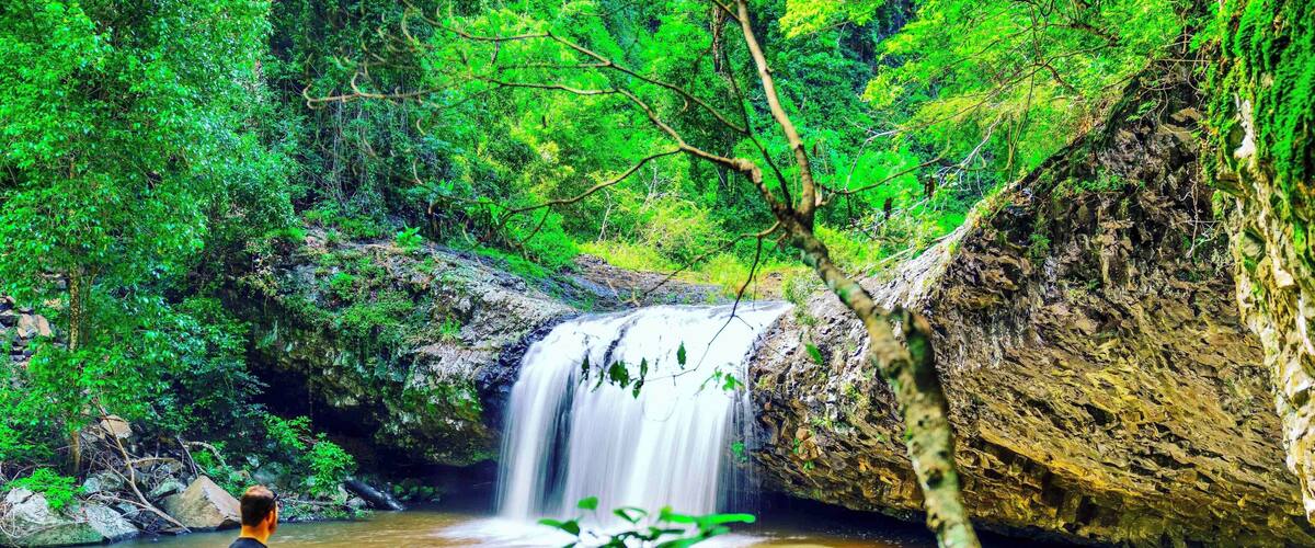 A waterfall in a forested area with a person standing on rocks.