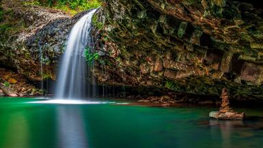 Une cascade se jetant dans un bassin d’eau claire et verdoyante, entouré de falaises rocheuses.