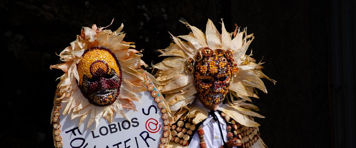 Two figures wearing elaborate masks and costumes with straw and beads.