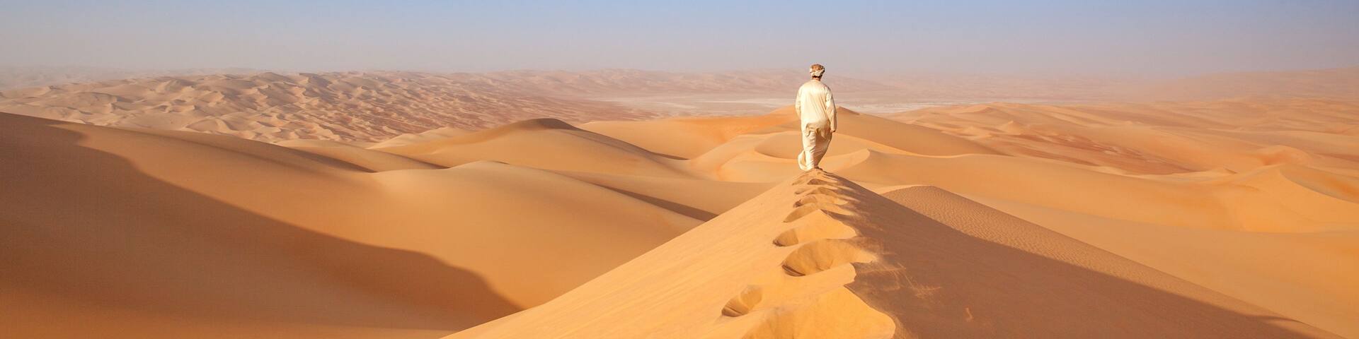 A person walking on a sand dune trail in a desert landscape.