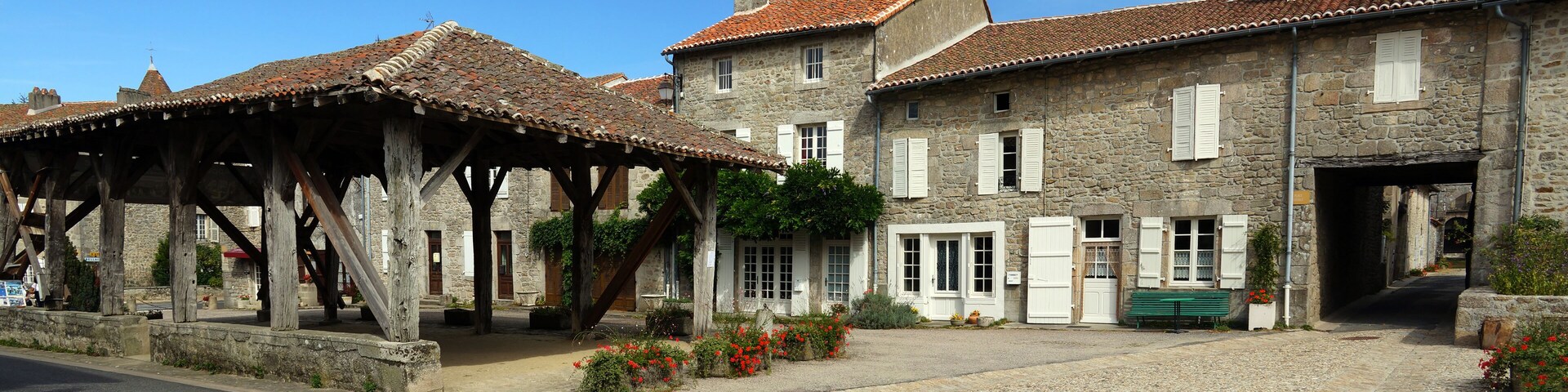 A stone building with a tiled roof, a wooden pavilion, and a cobblestone courtyard.