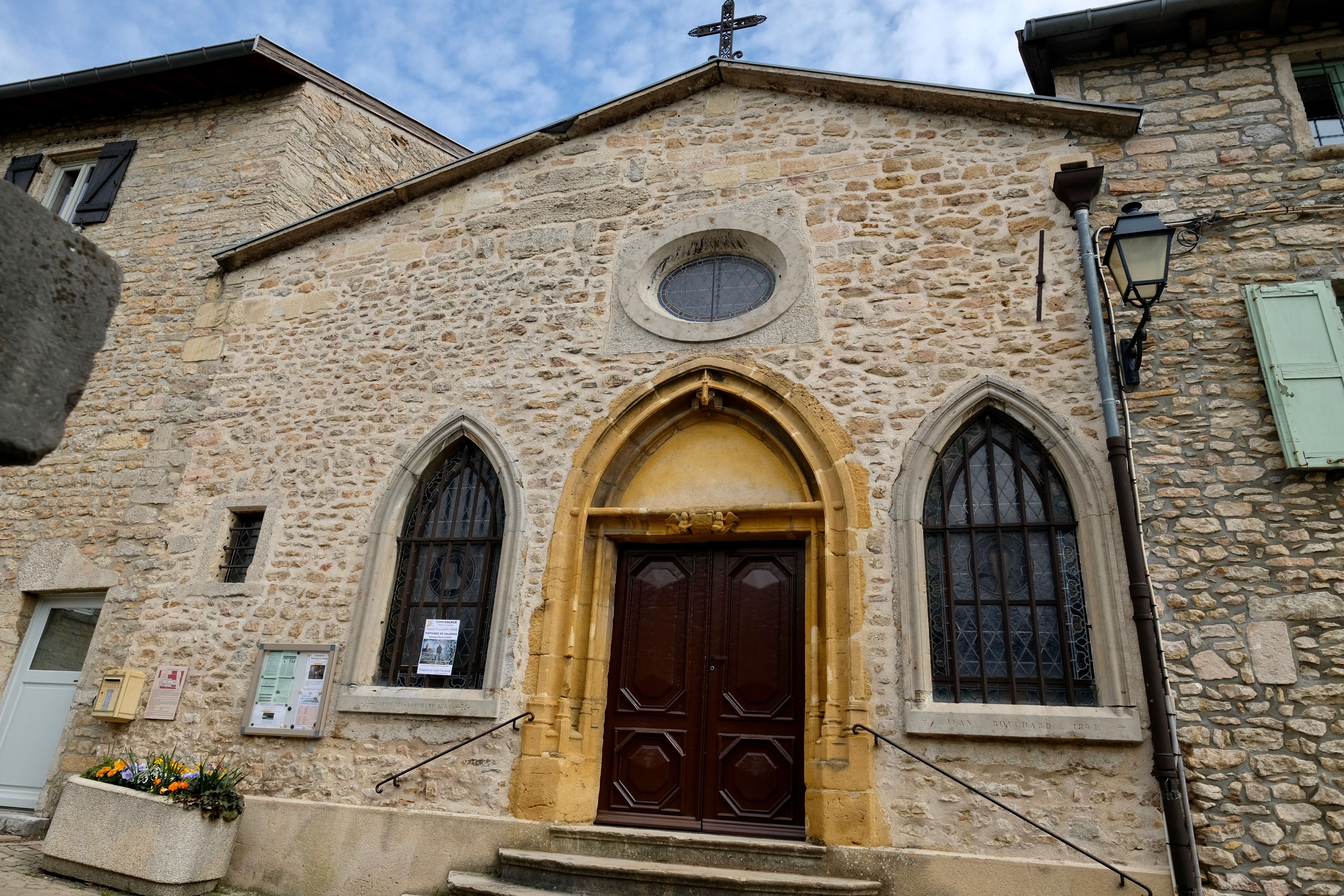 A stone church with a central arched doorway, two side windows, and a small circular window above the door.