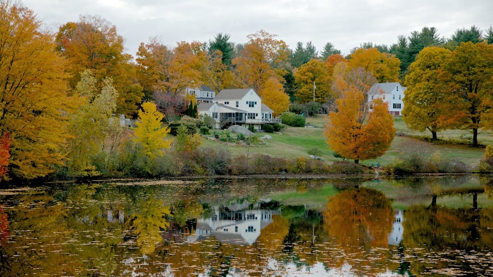 A house surrounded by autumn trees reflecting on a calm lake.