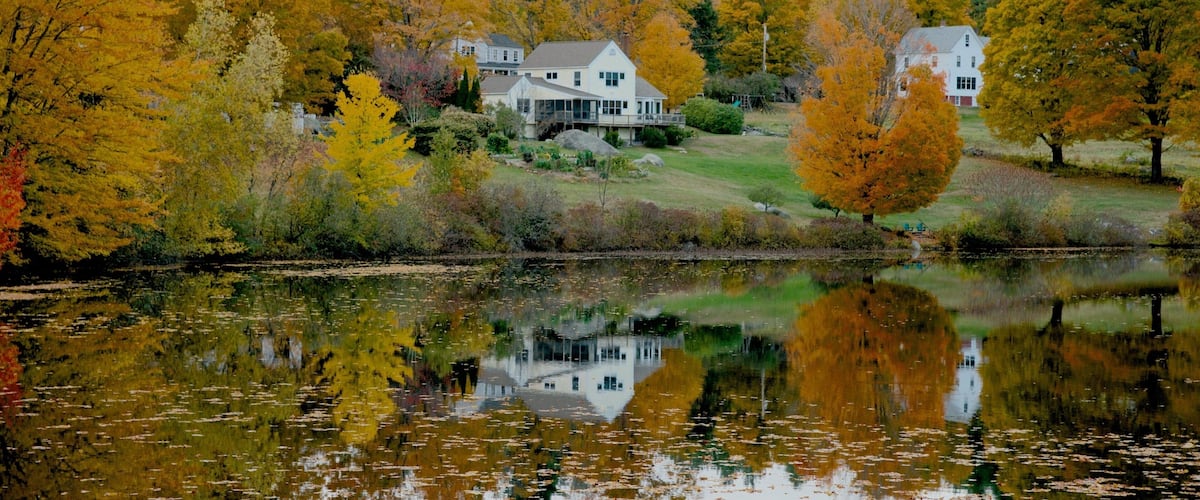 A house surrounded by autumn trees reflecting on a calm lake.