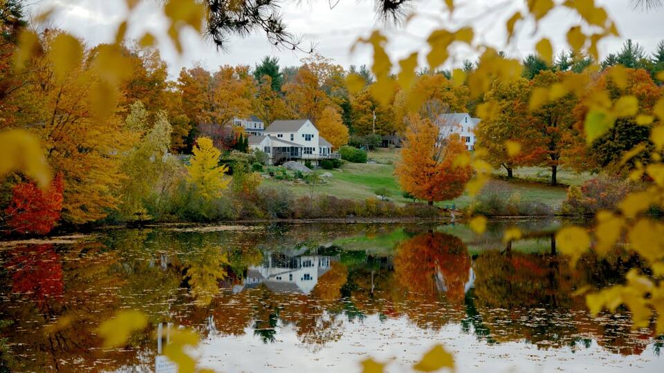 A house surrounded by autumn trees and a calm lake.