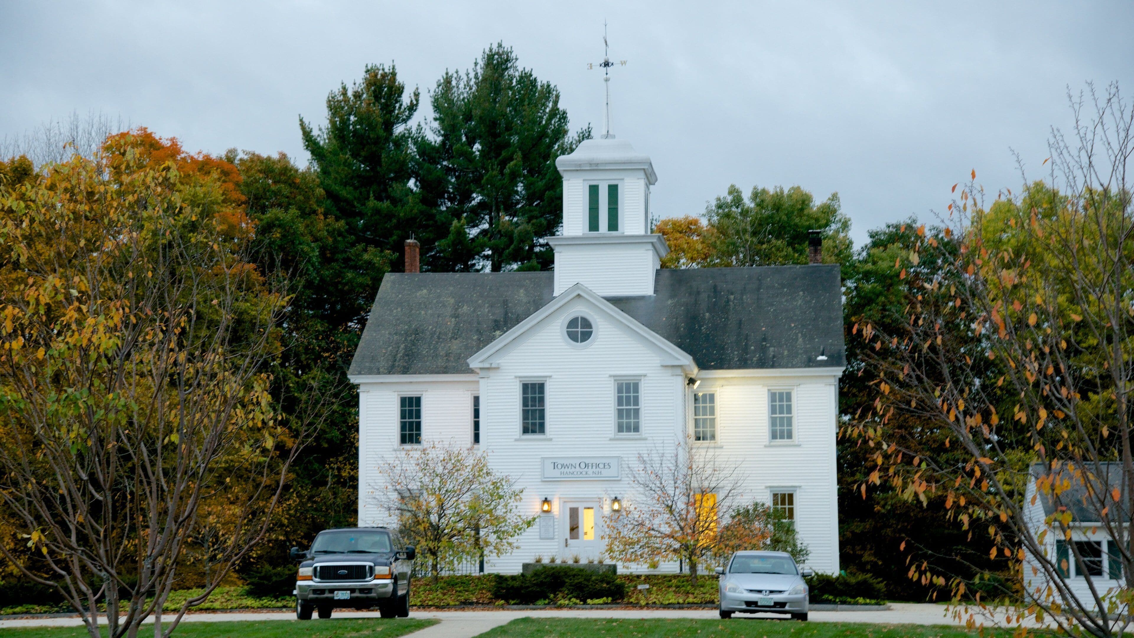A white building labeled "Town Offices" with a steeple, surrounded by trees with autumn leaves.