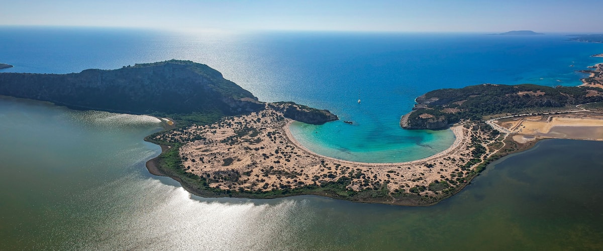 An aerial view of a coastal area with a curved bay, sandy beaches, and a small island with dense vegetation.