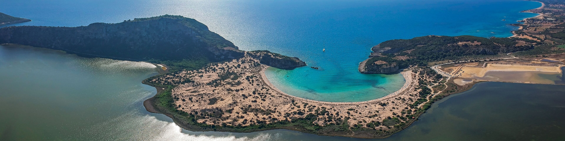 An aerial view of a coastal area with a curved bay, sandy beaches, and a small island with dense vegetation.