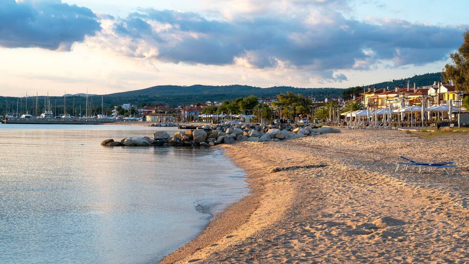 A beach with a rocky shoreline, boats, and buildings in the background.
