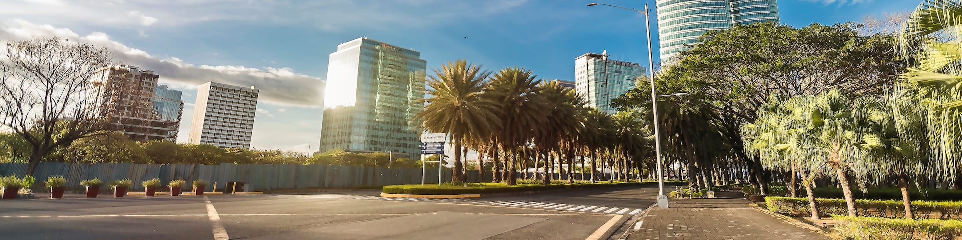 A cityscape with modern skyscrapers, a clear blue sky, and a well-maintained urban park with palm trees.