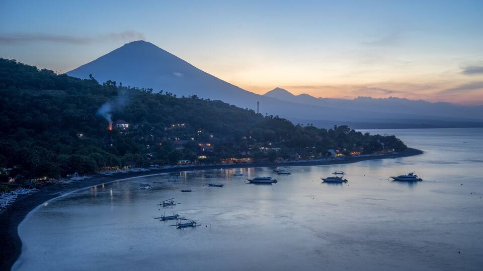 A coastal town with boats, a mountain, and a sunset.