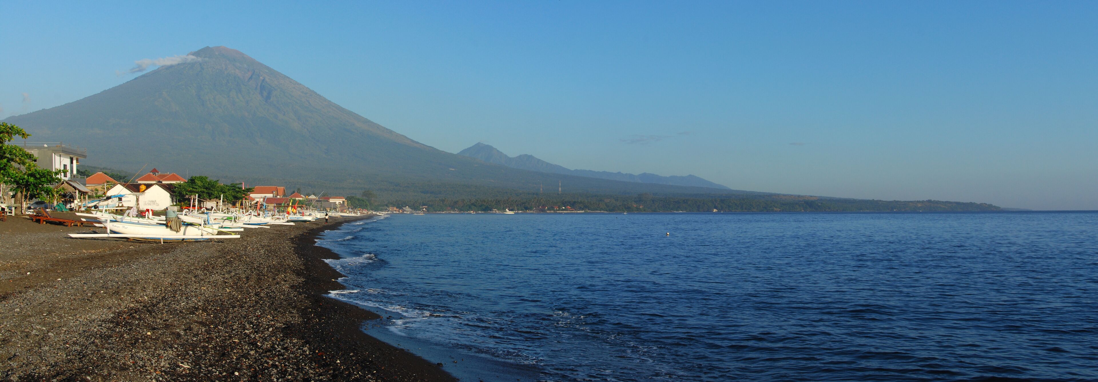 A beach with boats, a mountain, and a clear sky.