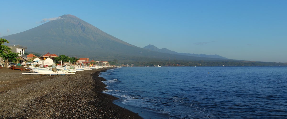 A beach with boats, a mountain, and a clear sky.