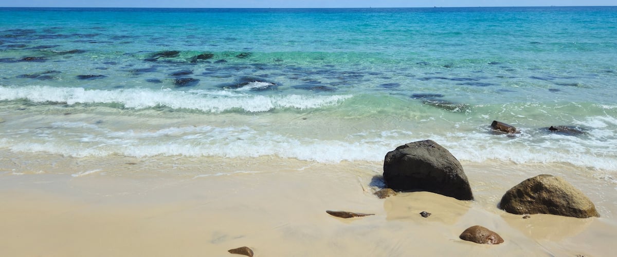 A beach with clear turquoise water, sandy shore, and scattered rocks.