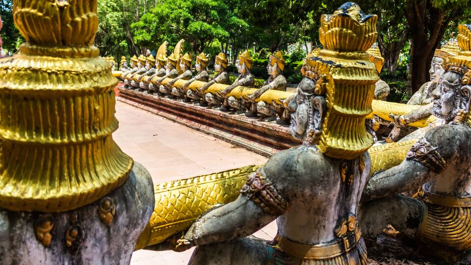 A row of golden statues with intricate designs, set against a backdrop of lush greenery.