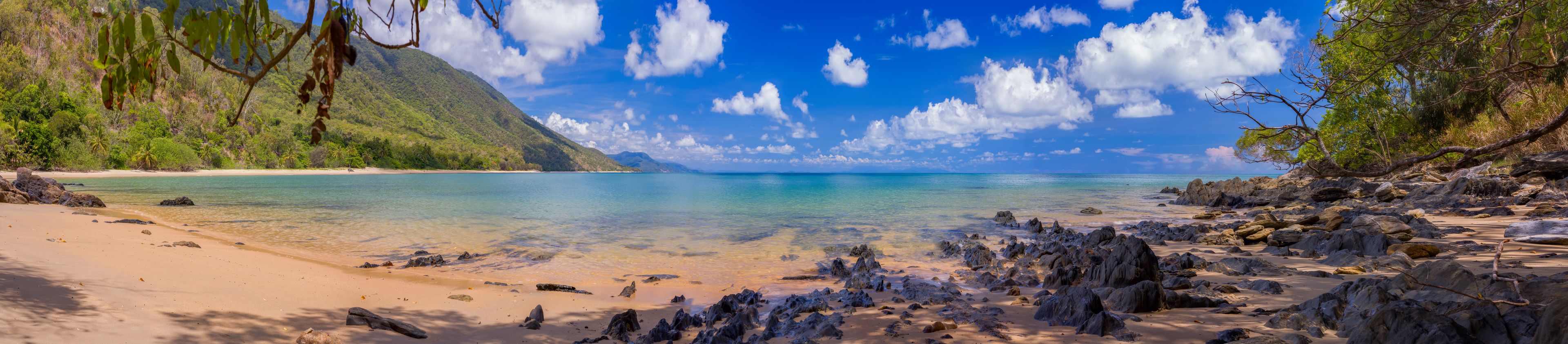 Une plage tropicale avec une eau turquoise et limpide, des rivages sablonneux et des affleurements rocheux.