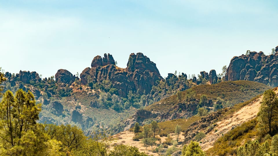 A rugged mountain landscape with prominent rock formations and scattered trees.