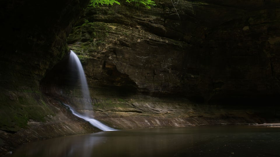 A waterfall cascading into a calm pool surrounded by rocky cliffs and lush greenery.