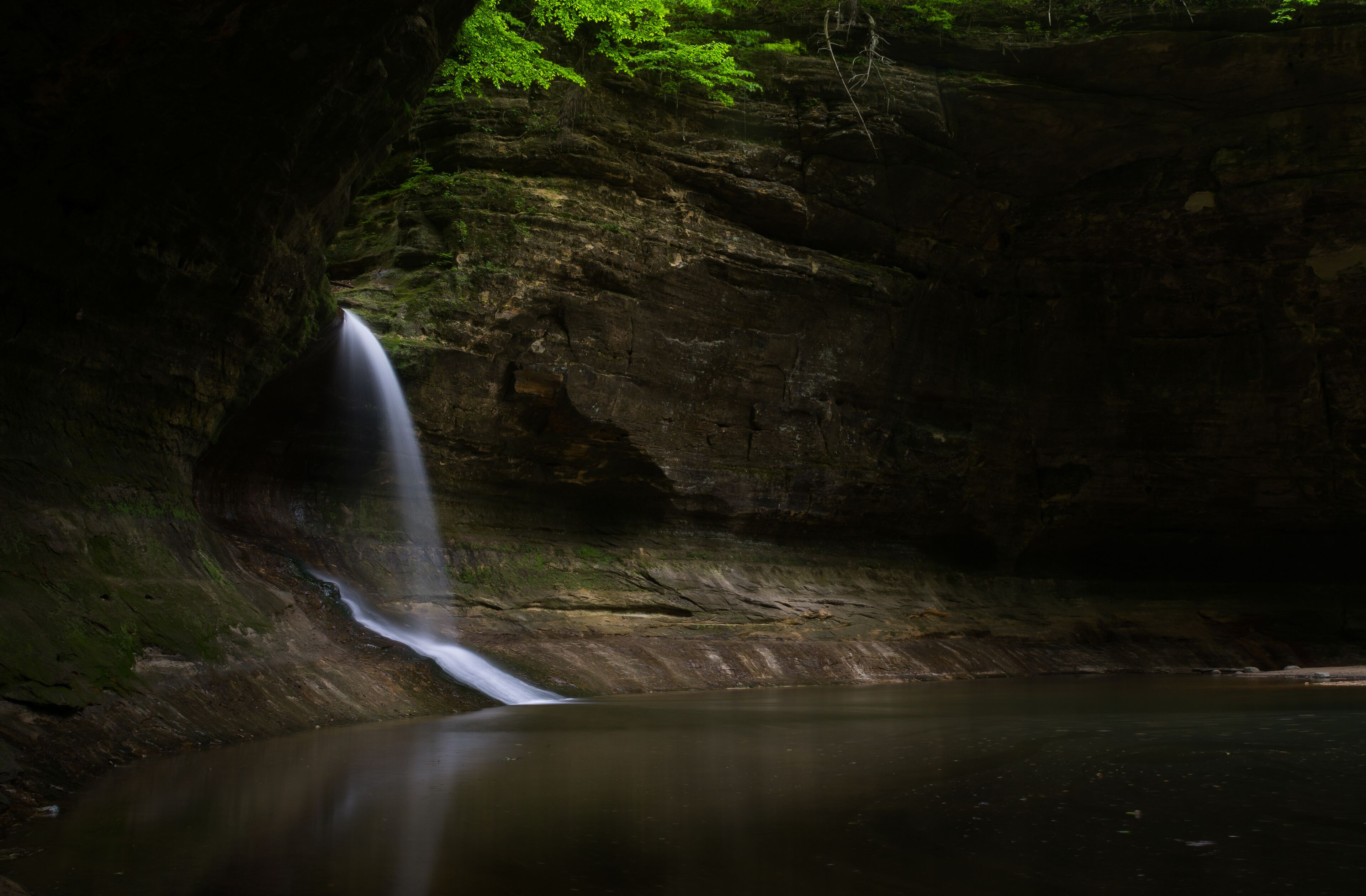 A waterfall cascading into a calm pool surrounded by rocky cliffs and lush greenery.