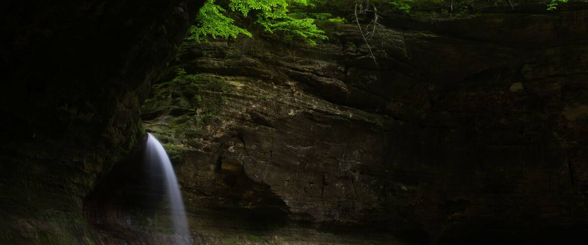 A waterfall cascading into a calm pool surrounded by rocky cliffs and lush greenery.