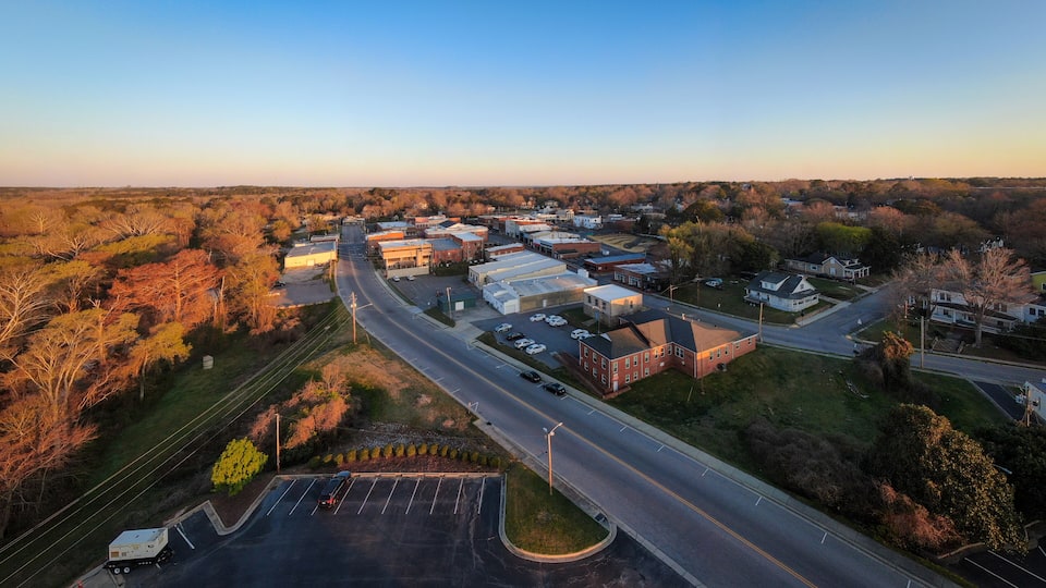An aerial view of a small town with a main road, parking lots, and various buildings.