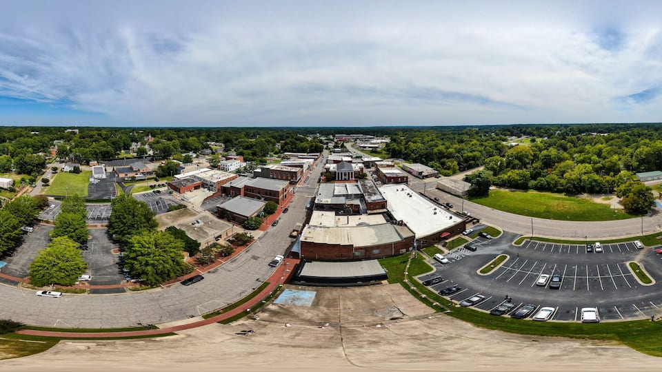 An aerial view of a town with a central roundabout, surrounding buildings, and green spaces.