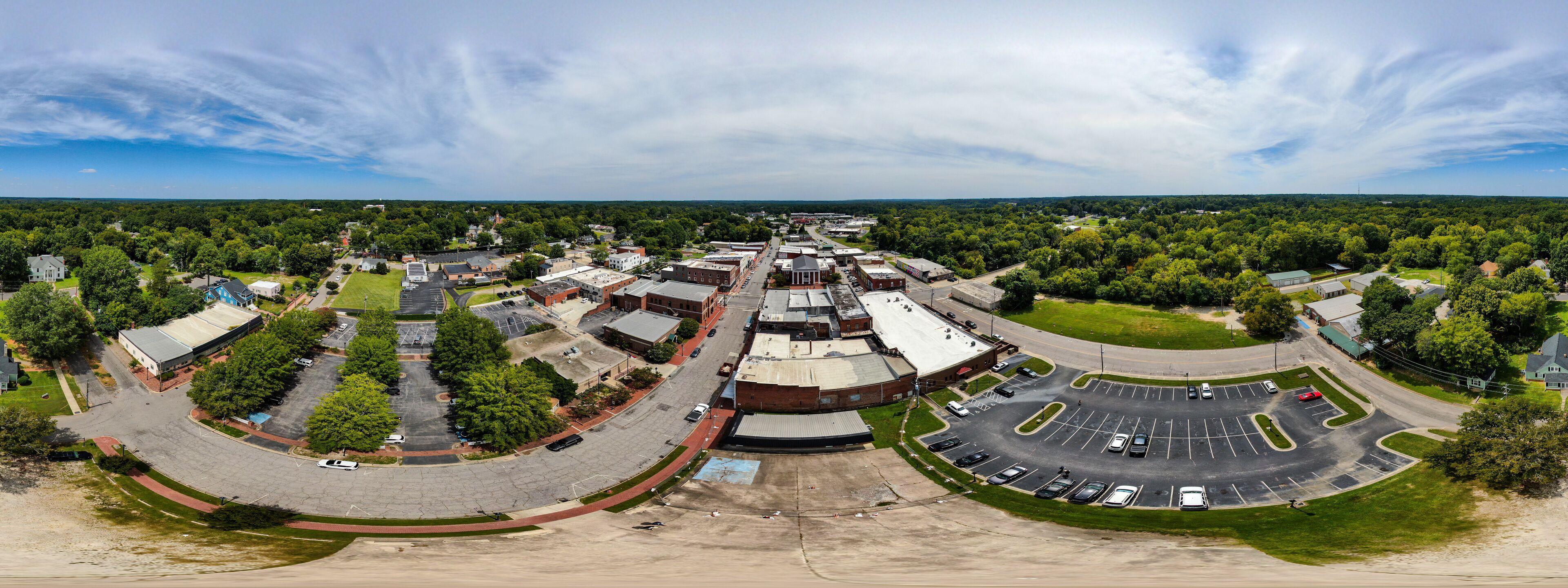 An aerial view of a town with a central roundabout, surrounding buildings, and green spaces.