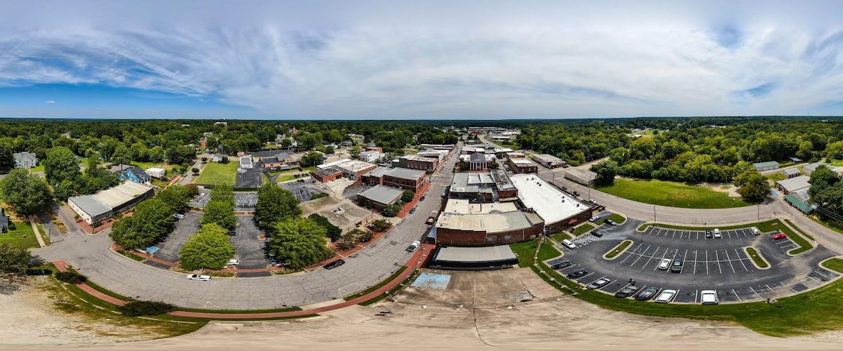 An aerial view of a town with a central roundabout, surrounding buildings, and green spaces.
