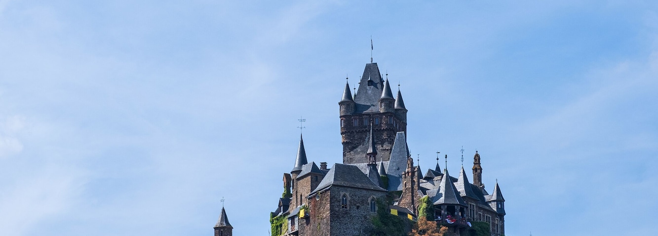 A castle on a hill with a small white building in the foreground.