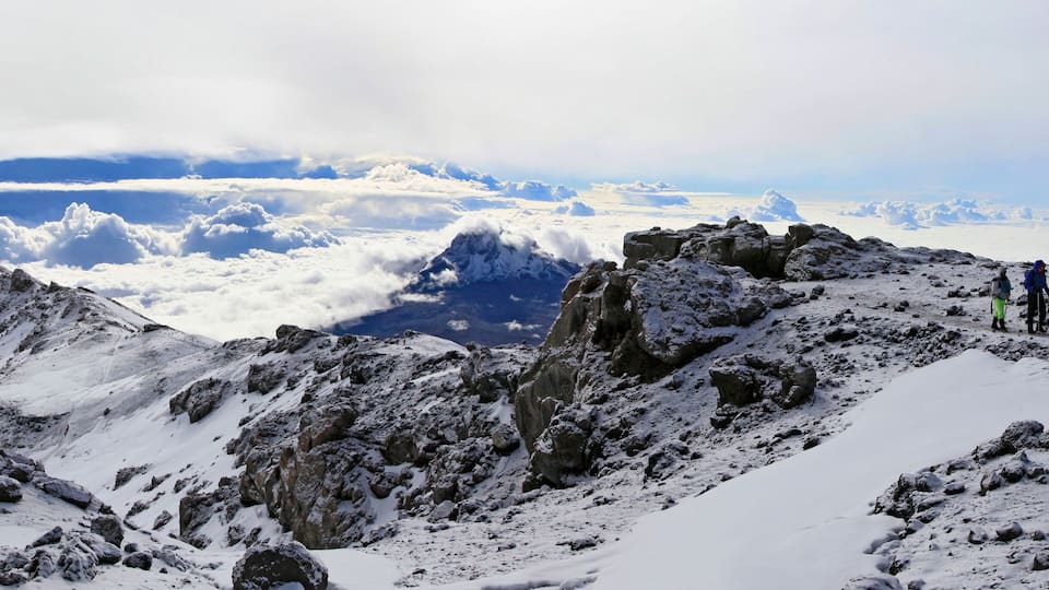 A snowy mountain peak with rocky terrain and a group of hikers.